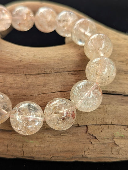 Macro photograph of 15mm Cherry Blossom Garden Quartz beads highlighting the water-clear matrix and delicate, pale pink hematite inclusions.