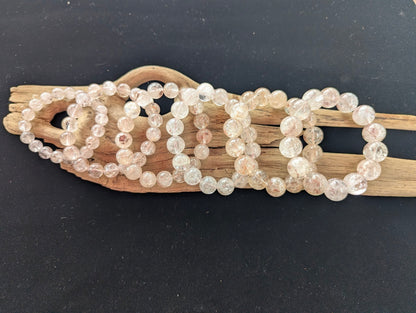 Suite of intuitively selected AAA Grade Brazilian Cherry Blossom Garden Quartz beaded stretch bracelets displayed on driftwood, showing calibrated sizes ranging from 10mm to 16mm.