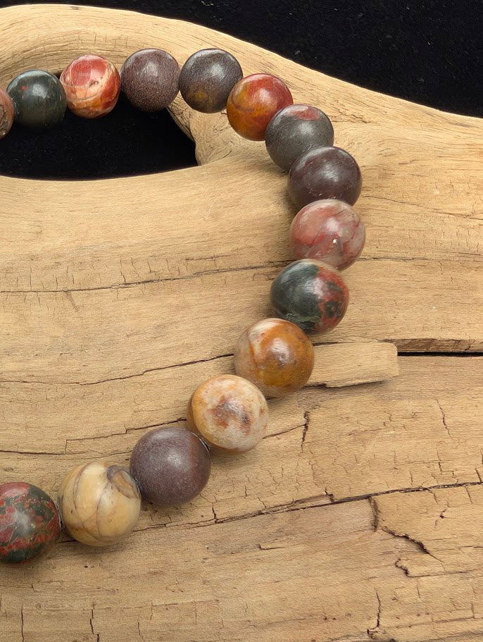 Macro close-up of 8mm polished Cherry Creek Jasper beads highlighting the high-gloss finish and natural red, green, and yellow brecciated patterns.