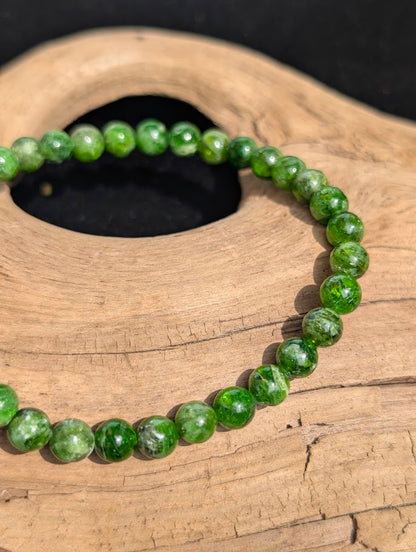Macro view of polished 4mm Chrome Diopside spherical beads on driftwood, highlighting the rich green coloration and natural internal cleavage planes.