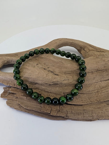 6.4mm Chrome Diopside bead bracelet from Siberia, Russia, showing vivid green color on natural driftwood.