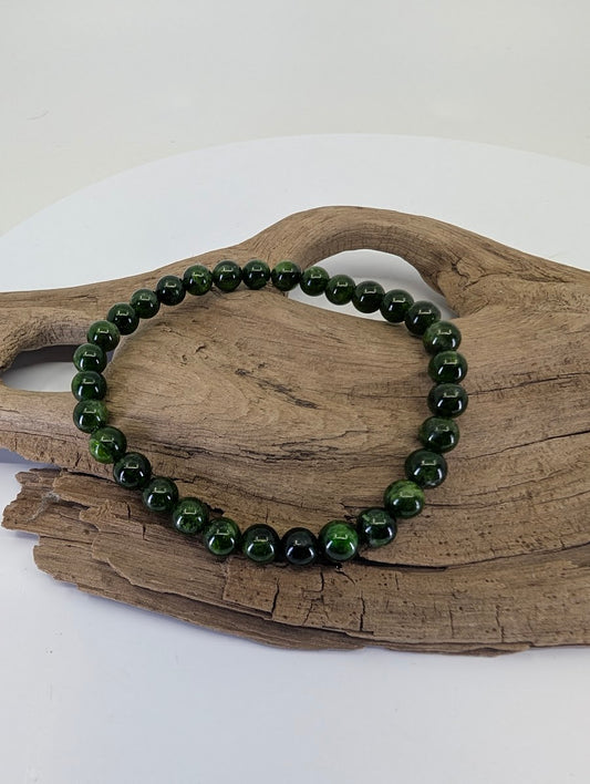 6.4mm Chrome Diopside bead bracelet from Siberia, Russia, showing vivid green color on natural driftwood.