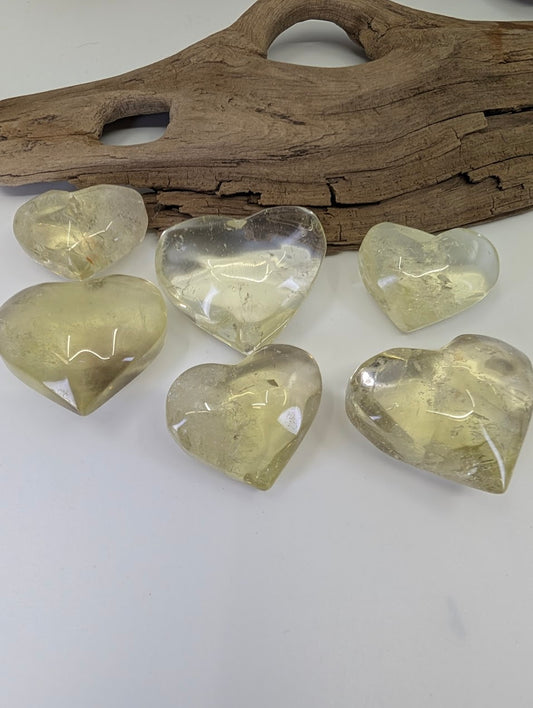 A collection of Natural Citrine Hearts from Congo displayed on a white surface with driftwood accent.