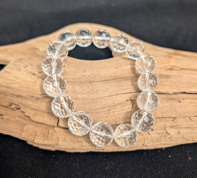 13mm faceted Clear Quartz beaded stretch bracelet resting on a driftwood display, showing high optical clarity.