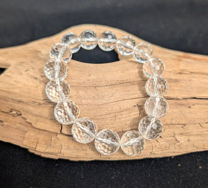 13mm faceted Clear Quartz beaded stretch bracelet resting on a driftwood display, showing high optical clarity.