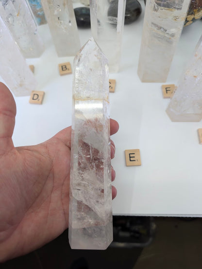 Hand holding the 20cm Clear Quartz tower (CQT-E) displaying exceptional clarity and high-polish finish.