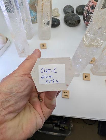 The unpolished hexagonal base of a 21cm Clear Quartz tower labeled CQT-C, 555g.