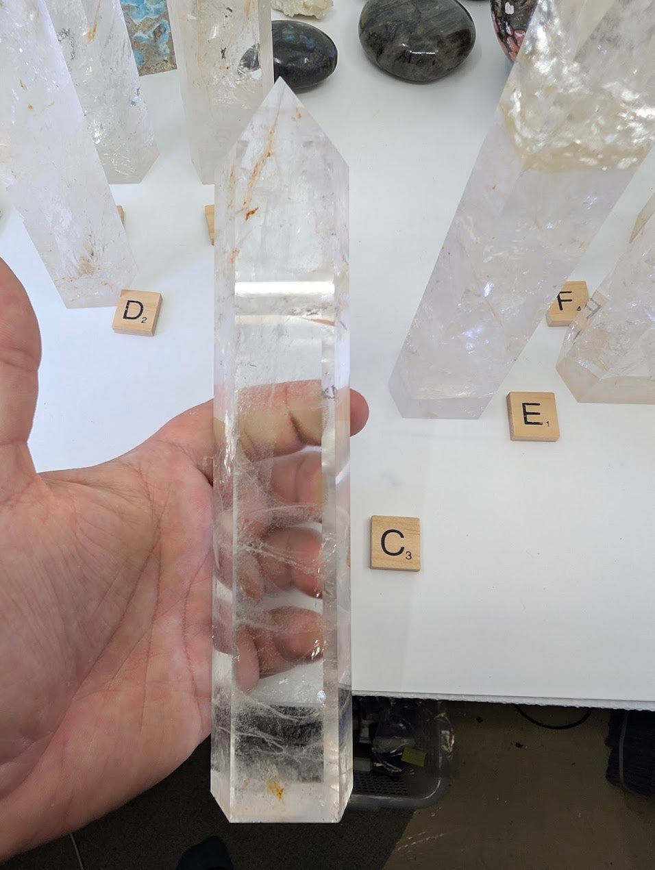 Hand holding the 21cm Clear Quartz tower (CQT-C) to highlight the dense frosted base transitioning to a clear point.