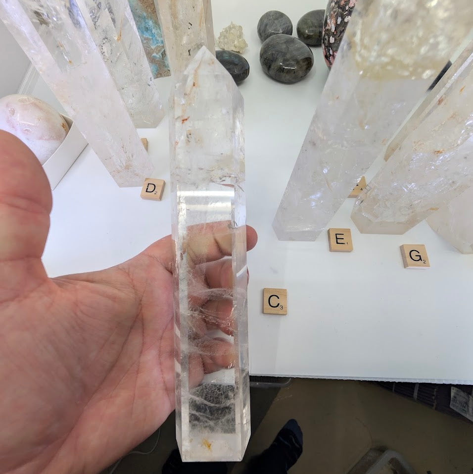 Hand holding the 21cm Clear Quartz tower (CQT-C) to highlight the dense frosted base transitioning to a clear point.