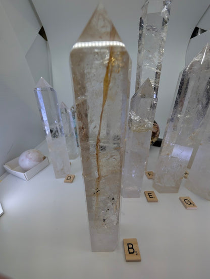 Polished 22cm Clear Quartz tower (CQT-B) standing upright, showcasing a prominent internal golden iron-oxide wisp.