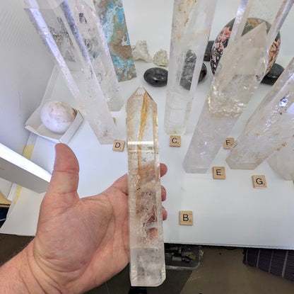 Hand holding the 22cm Clear Quartz tower (CQT-B) showing water-clear points and natural internal golden inclusions.
