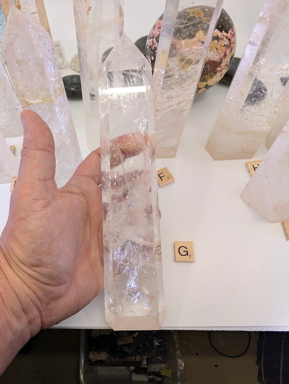 Hand holding the thick 23cm Clear Quartz obelisk (CQT-G) capturing internal light play and natural frosty sections.