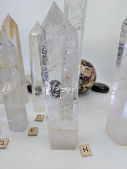 Polished 23cm Clear Quartz tower (CQT-H) standing up, showcasing dense internal structures and subtle golden inclusions.