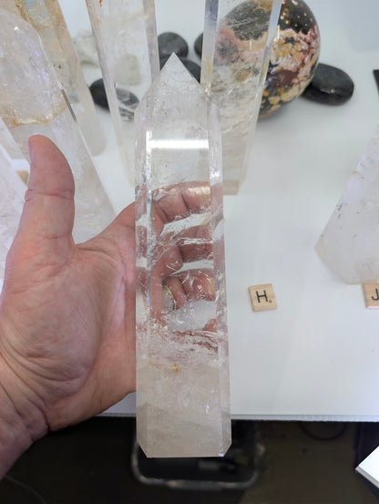 Hand holding the 23cm Clear Quartz tower (CQT-H) to reveal deep internal frosting and high exterior polish.