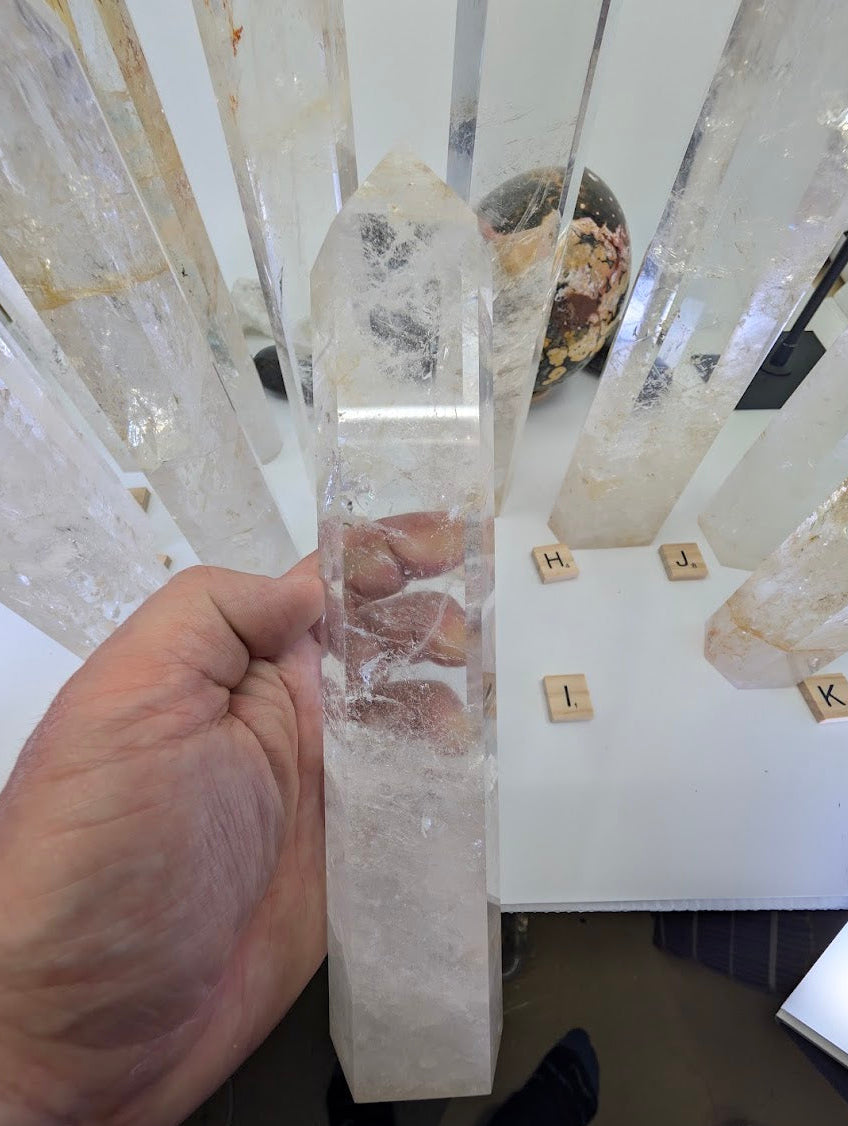 Hand holding the 24cm Clear Quartz obelisk (CQT-I) revealing a highly transparent upper point and cloudy base.