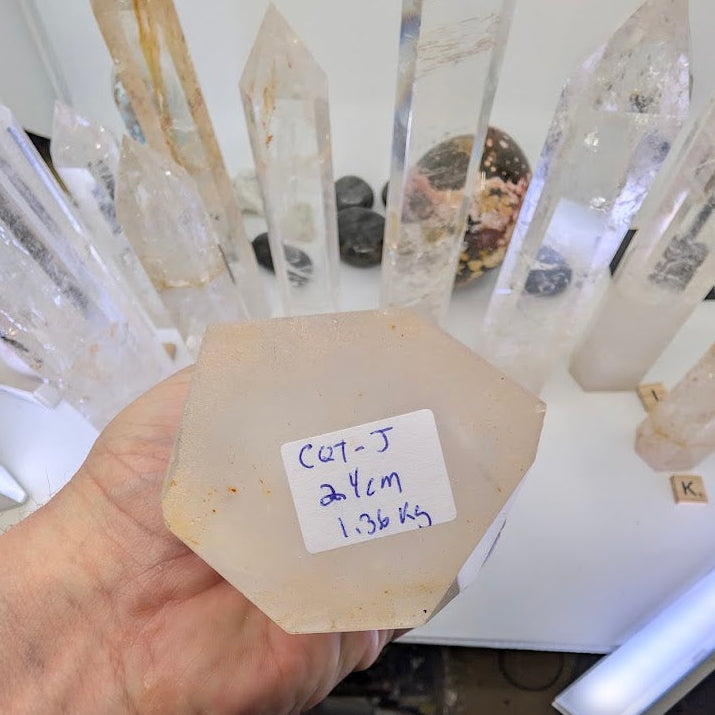The large unpolished hexagonal base of a 24cm Clear Quartz tower labeled CQT-J, 1.36kg
