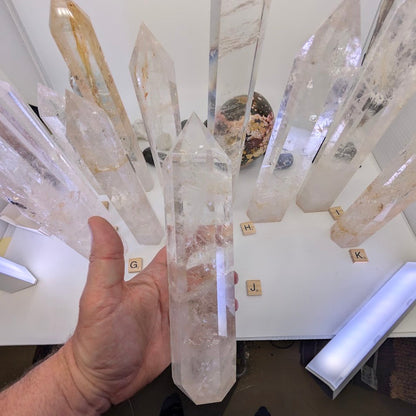 Hand holding the heavy 24cm Clear Quartz obelisk (CQT-J), demonstrating its scale and thick frosted base.