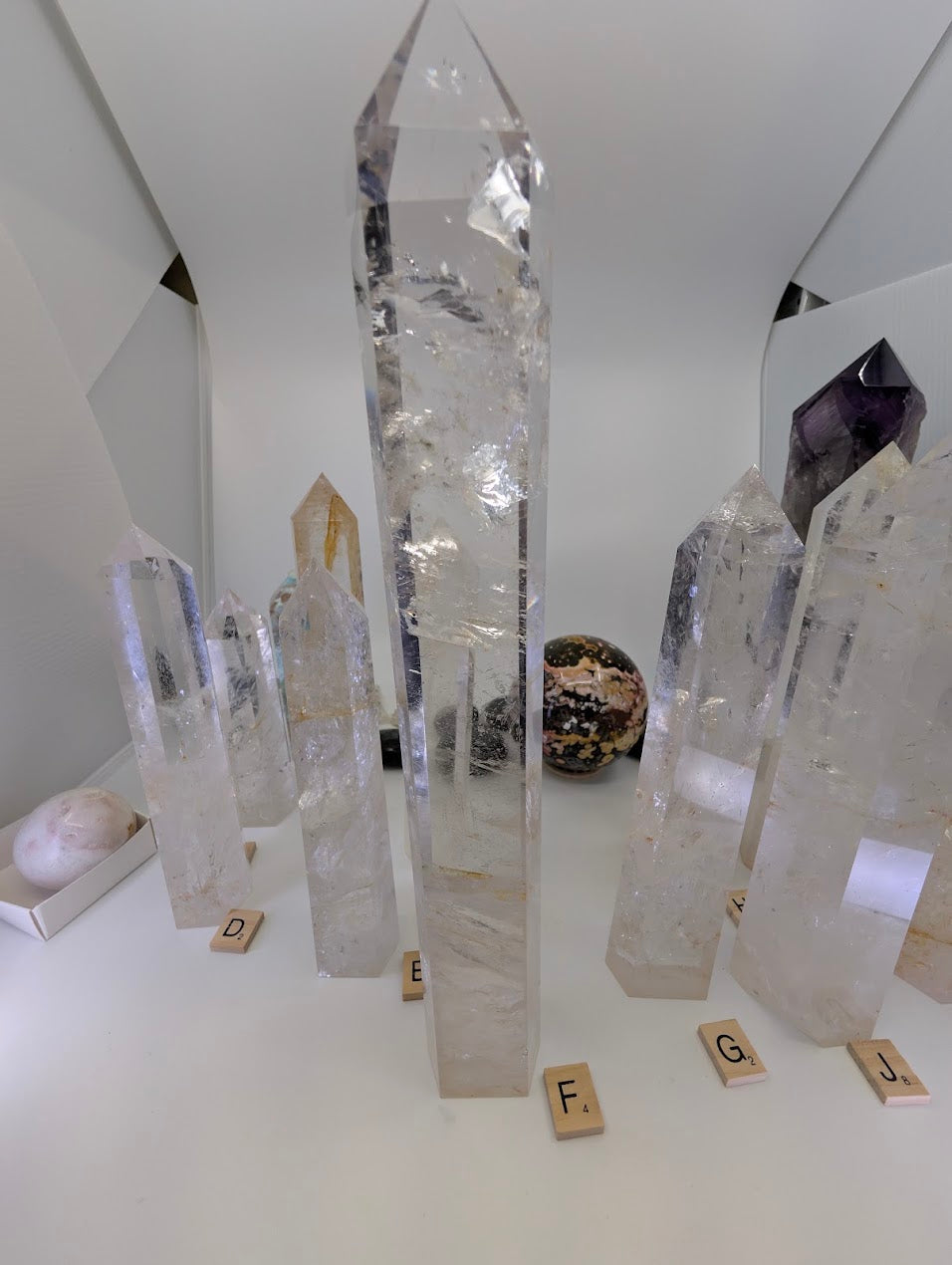 A massive 31cm polished Clear Quartz tower (CQT-F) towering above others, showing layered internal veiling.
