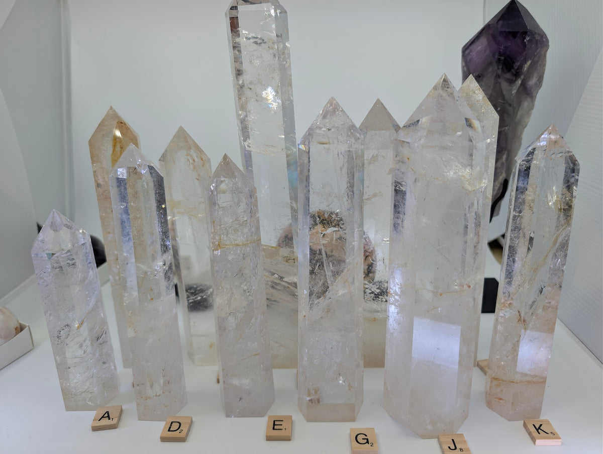 A diverse group of polished AA-grade Clear Quartz towers featuring high clarity, internal veils, and golden iron-oxide inclusions.