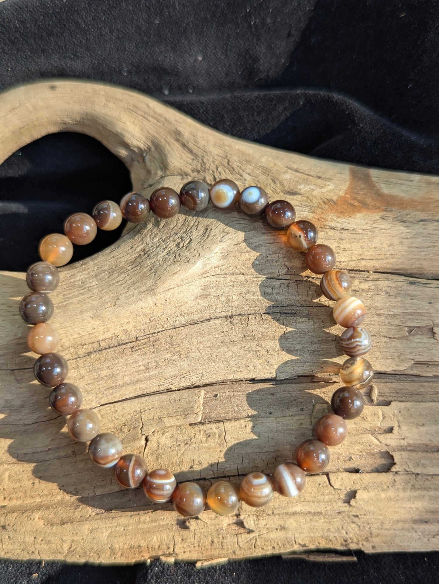A 6mm Coffee Agate round bead stretch bracelet positioned on a flat neutral presentation surface, demonstrating exceptional lapidary polish and deep espresso brown mineral banding.