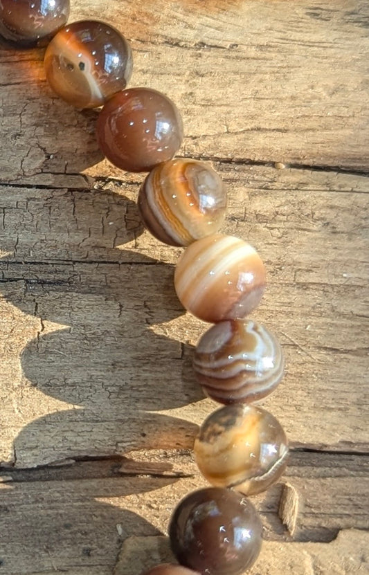 Macro close-up view of polished 6mm Coffee Agate spheres on a dark background, highlighting the glass-like luster and natural concentric chocolate and cream bands.