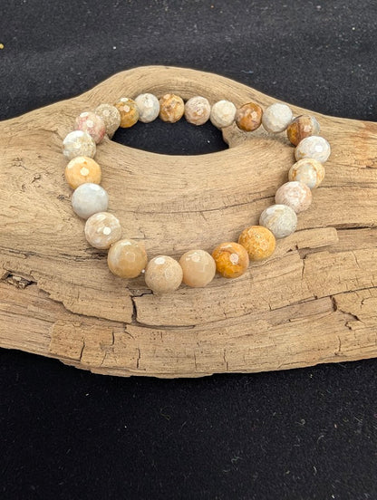 8mm faceted Coral Jade beaded stretch bracelet resting on a driftwood display, showing earthy peach, tan, and cream fossil patterns.