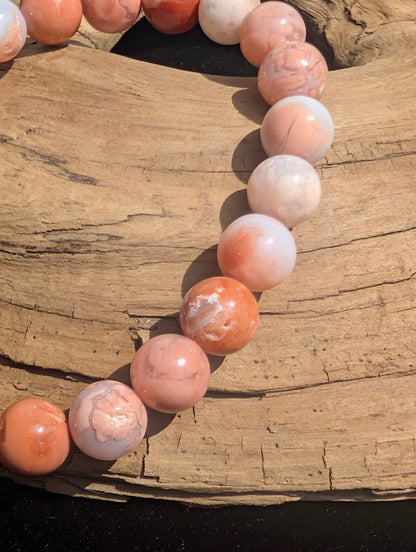 Macro view of 8mm Cotton Candy Agate beads on natural wood, displaying salmon-pink colouration, white banding, and minor natural vugs.