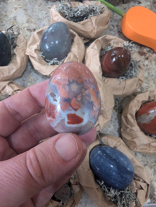 A 2-inch polished Cotton Candy Agate egg held in a hand, displaying complex brecciated patterns of pink, peach, white, and translucent grey with a small natural vug.