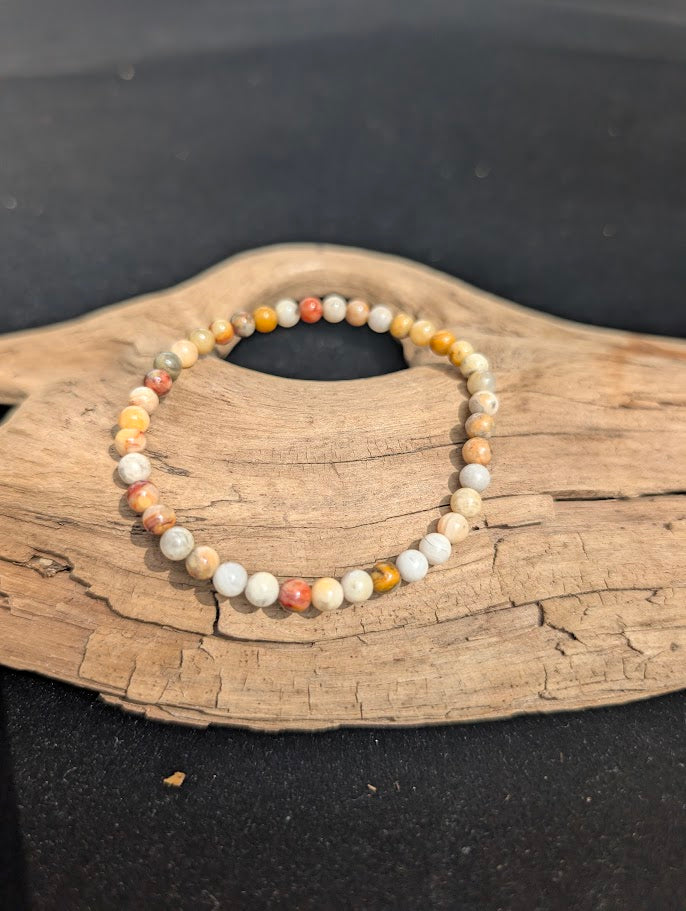 A 4mm Crazy Lace Agate beaded bracelet resting on natural driftwood, displaying complex cream, yellow, and orange banding.