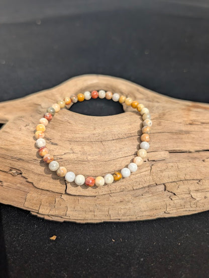 A 4mm Crazy Lace Agate beaded bracelet resting on natural driftwood, displaying complex cream, yellow, and orange banding.
