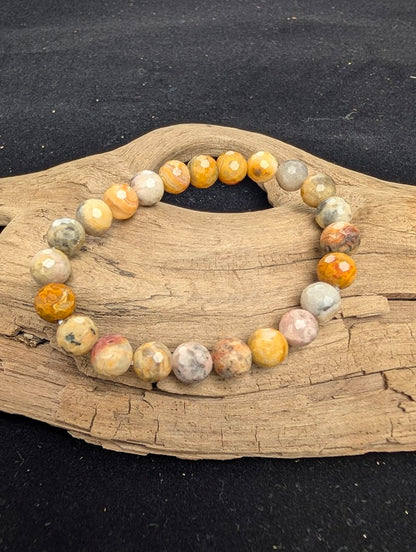 8mm faceted Crazy Lace Agate beaded stretch bracelet resting on a driftwood display, showing multi-coloured yellow, grey, and cream banded stones.