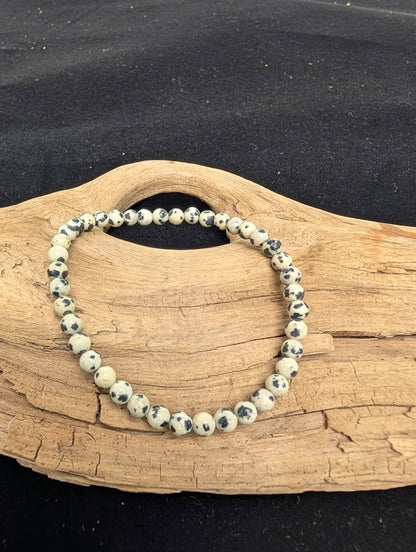 4mm polished Dalmatian Jasper beaded stretch bracelet resting on a driftwood display, showing a creamy pale matrix with distinct black spots.