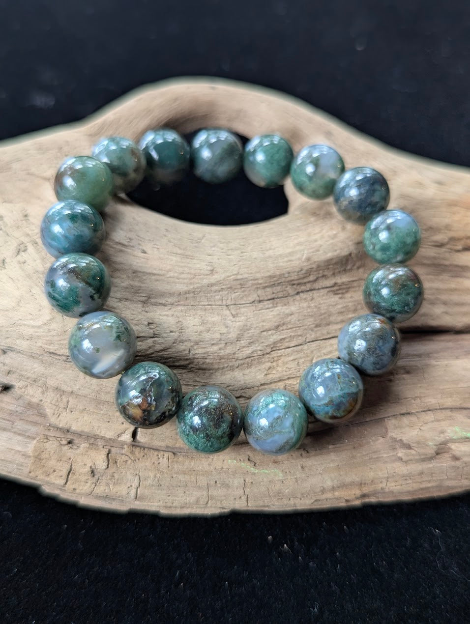 12mm High-Quality Dark Moss Agate statement bracelet showcased on a rustic driftwood surface.