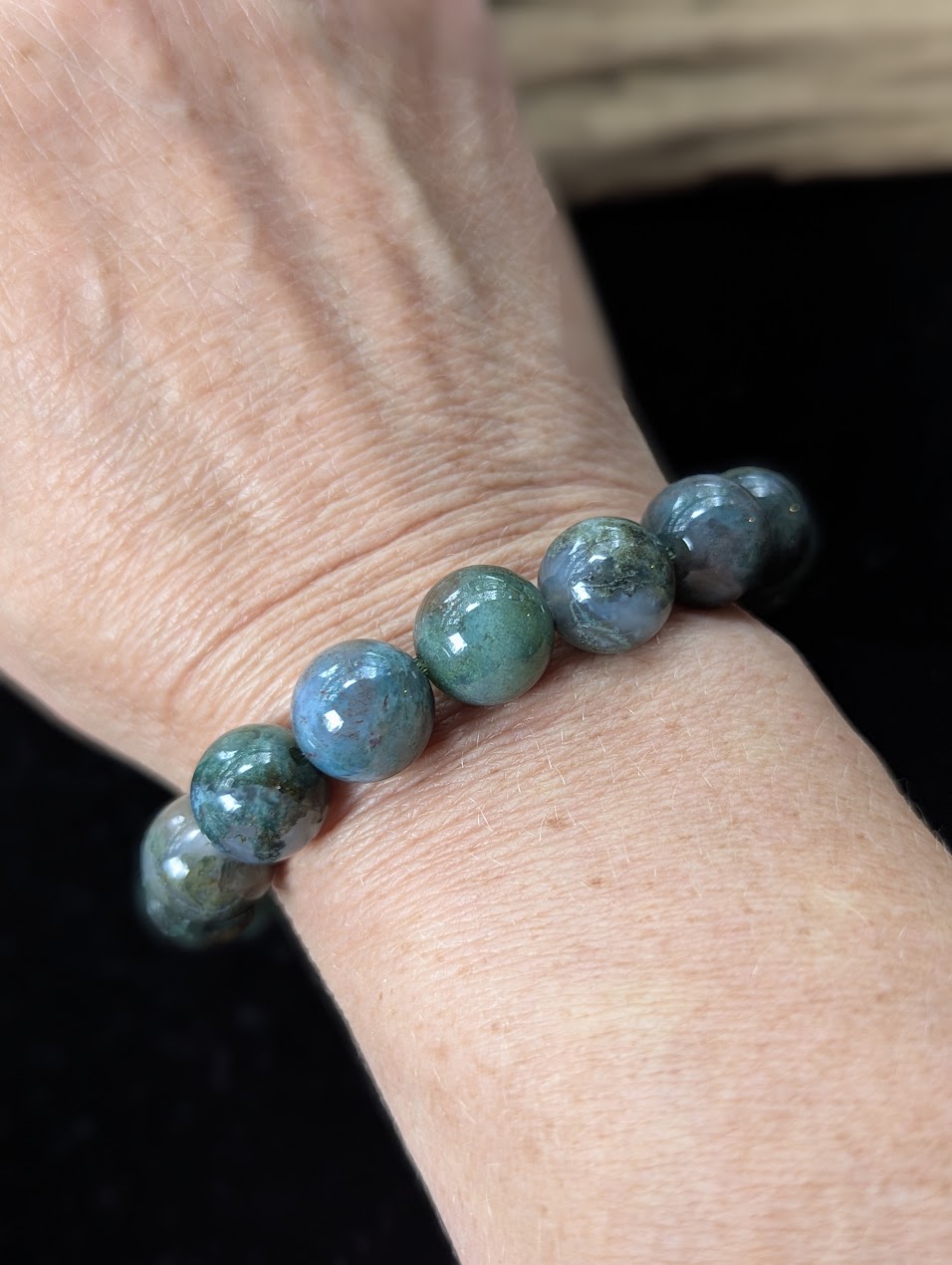 Substantial 12mm Dark Moss Agate gemstone bracelet worn on a wrist, highlighting its prominent collector profile.