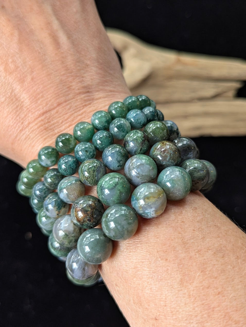 Multiple Dark Moss Agate beaded bracelets stacked together on a wrist, showcasing the full range of bead sizes from 8mm to 13mm.