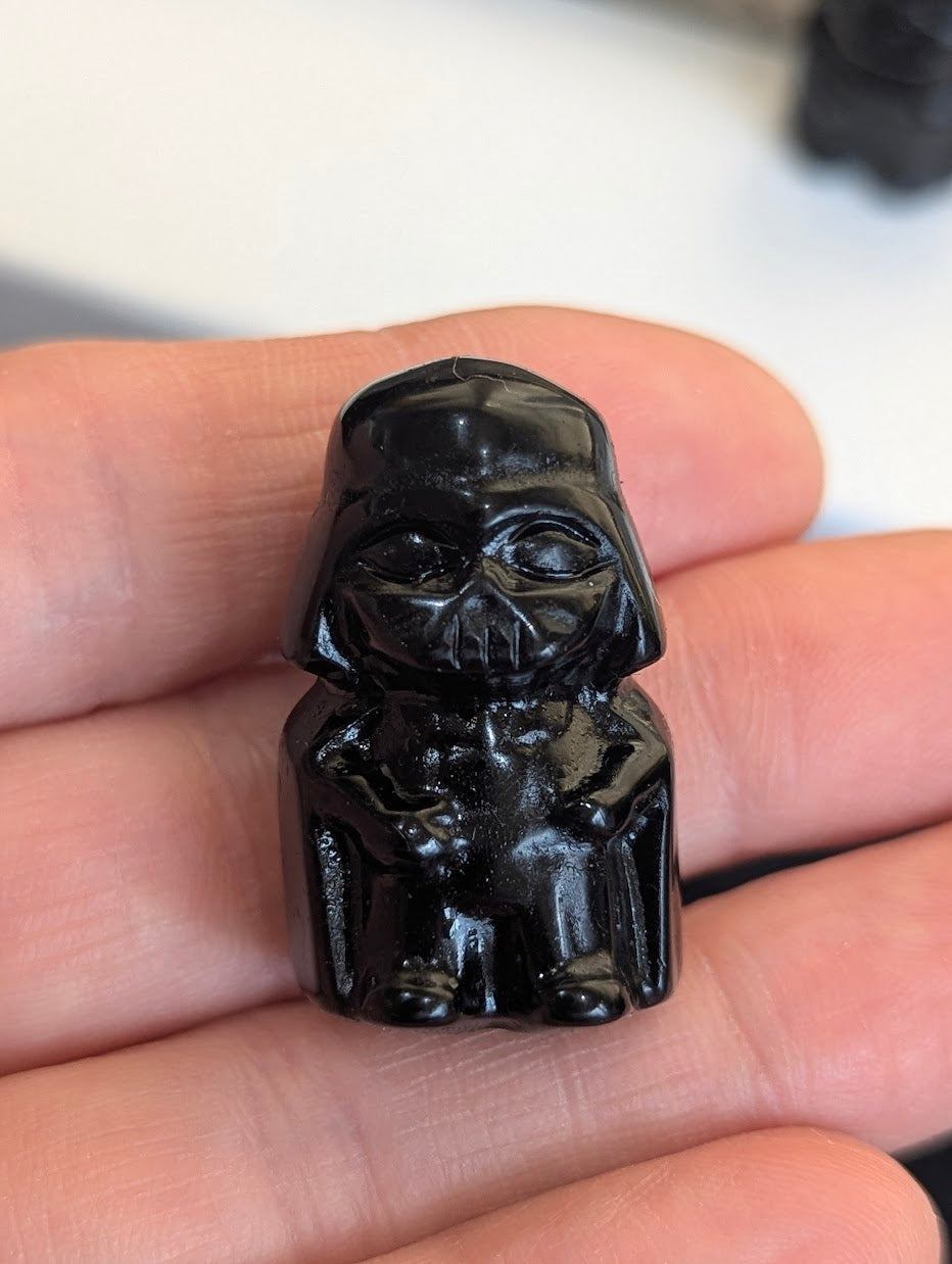 Front view of a tiny 3cm Black Obsidian Darth Vader carving held in a hand.