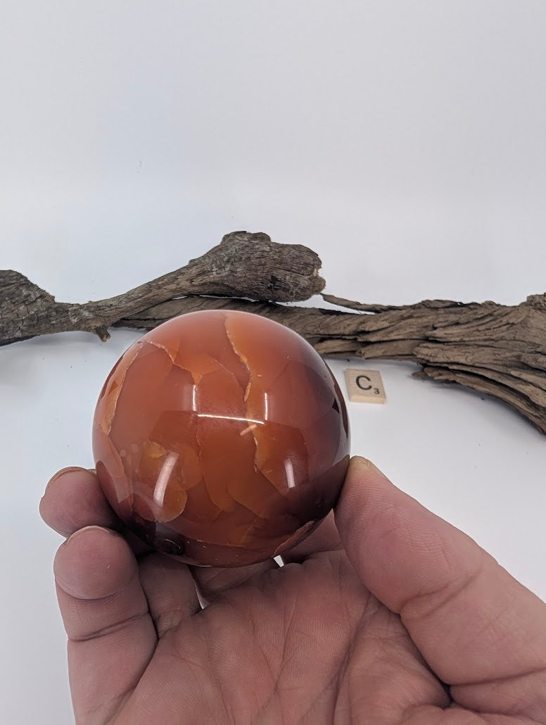 Rich carnelian-colored Mookaite sphere held in hand.