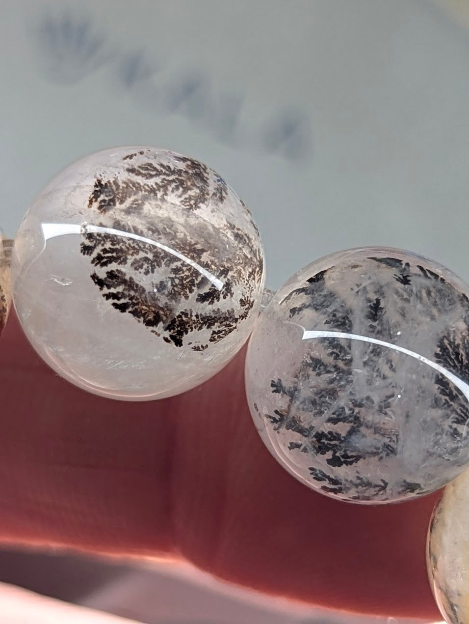 Two clear gemstones with black inclusions held by a hand against a blurred background