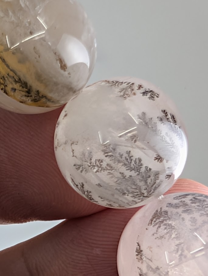 Assorted dendritic quartz beads arranged to showcase internal tree-like manganese formations.