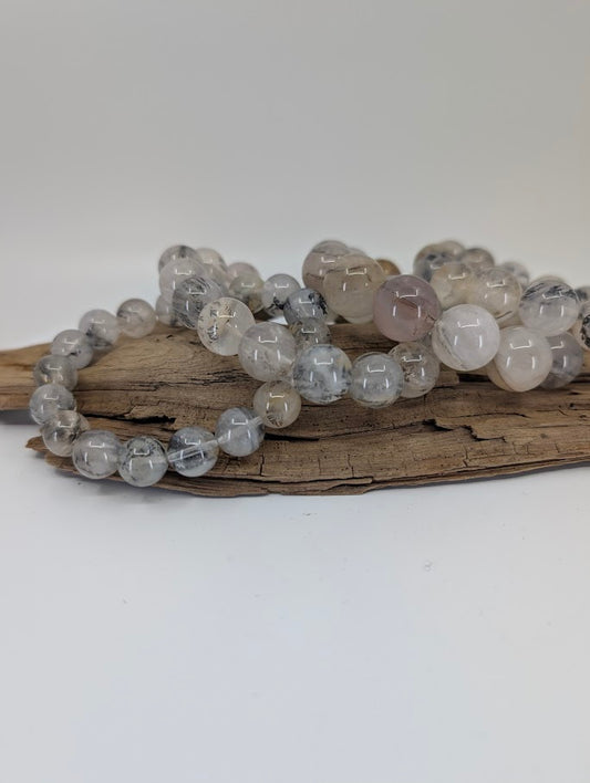 Assorted dendritic quartz bracelets in multiple bead sizes displayed on wooden stand.