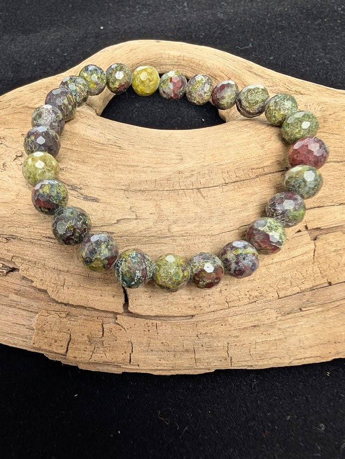 8mm faceted Dragon Blood Stone beaded stretch bracelet resting on a driftwood display, showing contrasting earthy green and deep red colouration.