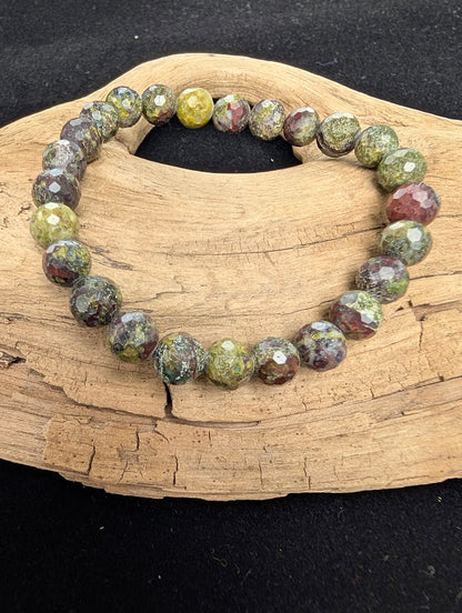 8mm faceted Dragon Blood Stone beaded stretch bracelet resting on a driftwood display, showing contrasting earthy green and deep red colouration.