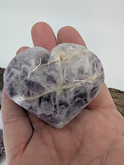 Hand holding a medium purple Dream Amethyst heart showing polished texture.