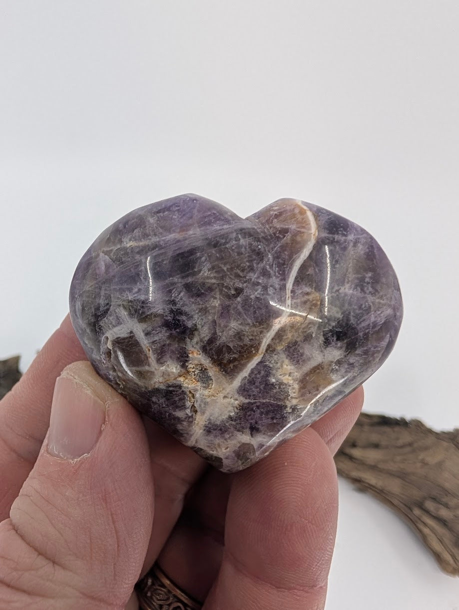 Hand holding a small purple Dream Amethyst heart showing polished texture.