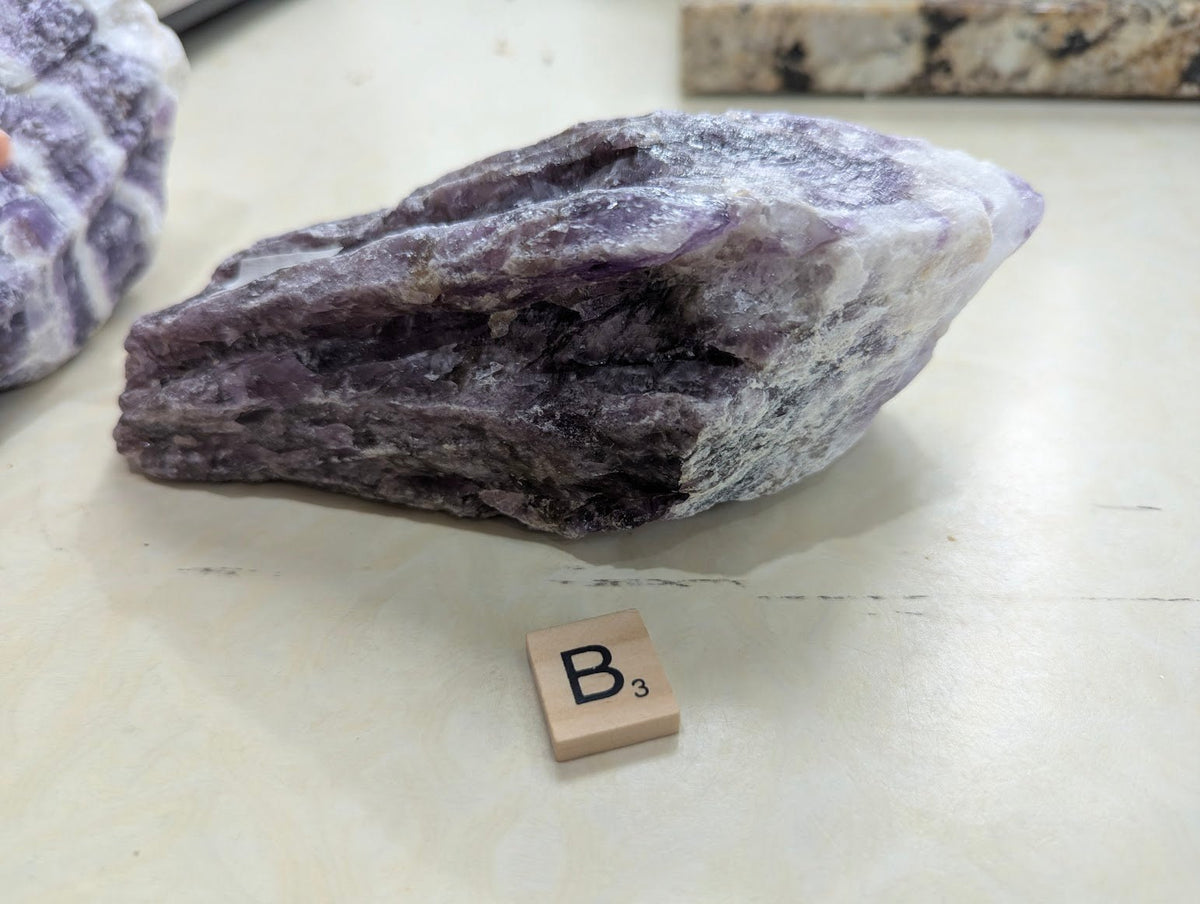 Horizontal display of a raw Dream Amethyst specimen, showing natural cleavage planes and dark purple color.