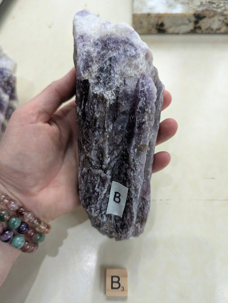 Raw Dream Amethyst chunk held vertically in hand, showing deep purple saturation and natural rough surface.