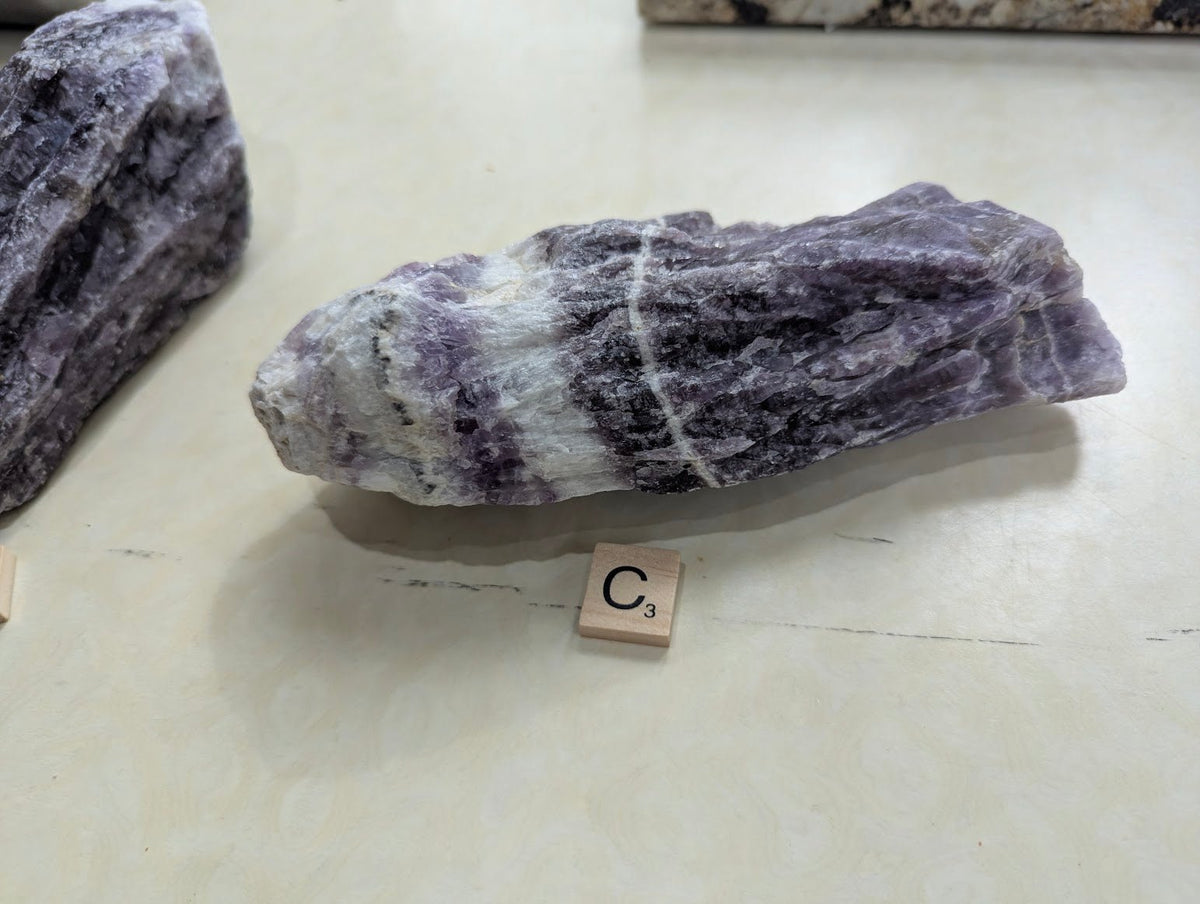 Raw Dream Amethyst chunk resting horizontally, showing striking white quartz veins cutting through the purple mineral.