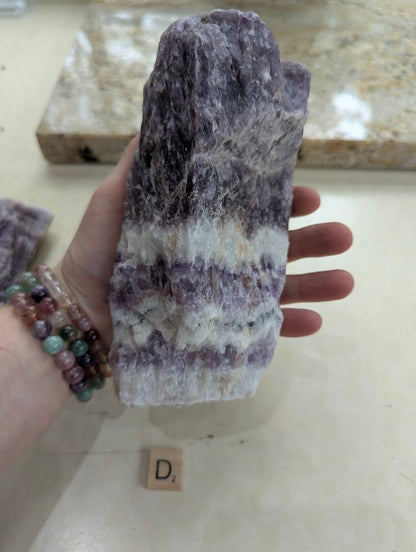 Hand displaying a large Dream Amethyst chunk, showing horizontal chevron banding across the natural raw surface.