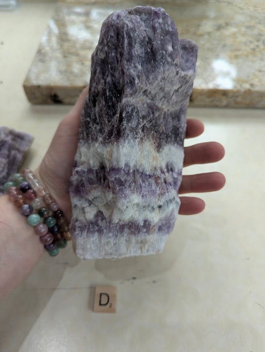Hand displaying a large Dream Amethyst chunk, showing horizontal chevron banding across the natural raw surface.
