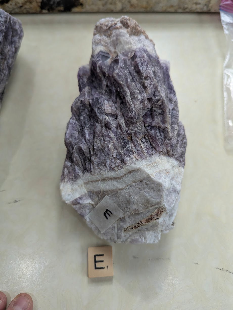 Raw Dream Amethyst specimen, showing a rugged natural texture and a thick band of white quartz at the lower edge.